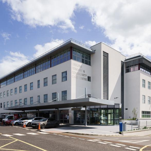Located adjacent to the listed maternity building within the Lagan Valley Hospital complex, the design comprises a four storey building and adjacent car park on the steeply sloping site, set on a plinth which integrates into the ground at the main entrance.